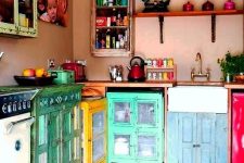 a boho maximalist kitchen with dusty pink walls, colorful mismatching cabinets and colorful cookware is amazing