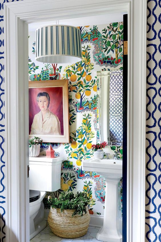 a bold maximalist bathroom with fruit print wallpaper, a striped lamp, potted greenery, a bold artwork and vintage-inspired appliances