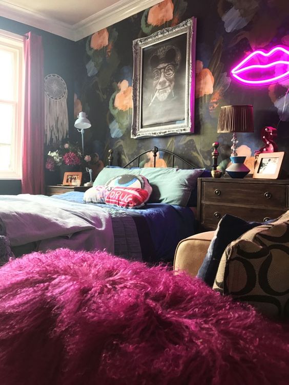 A bold maximalist bedroom with a dark floral accent wall, a metal bed, mid century modern dressers, bold bedding and a neon light