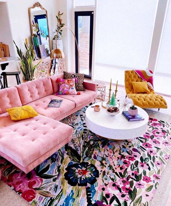 a bold maximalist living room with a colorful floral rug, a pink sofa, a yellow lounger and bright pillows and accessories