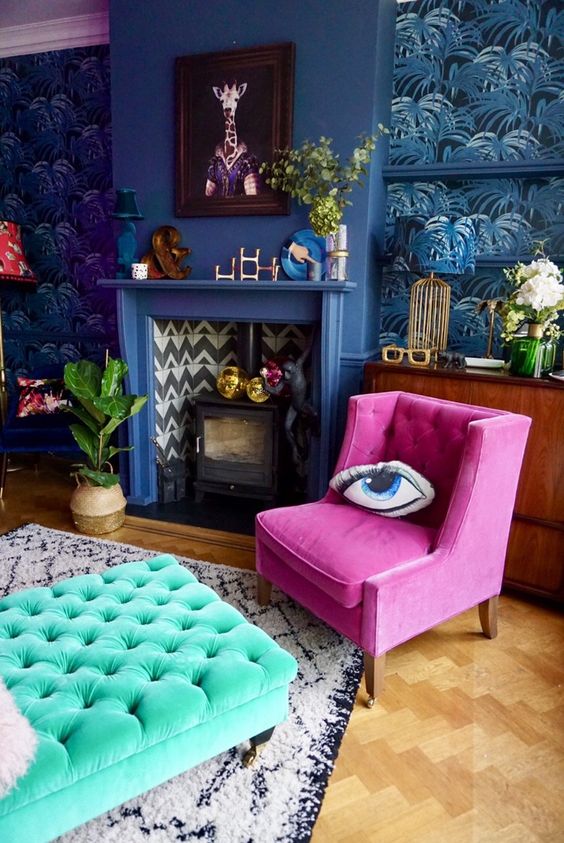 a bold maximalist living room with tropical leaf wallpaper, a blue fireplace, a fuchsia chair and a turquoise ottoman, bold art and decor