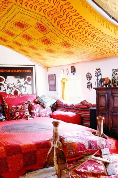 a bold maximalist space with pink walls, a wooden furniture, colorful bedding and pillows, a yellow canopy over the space