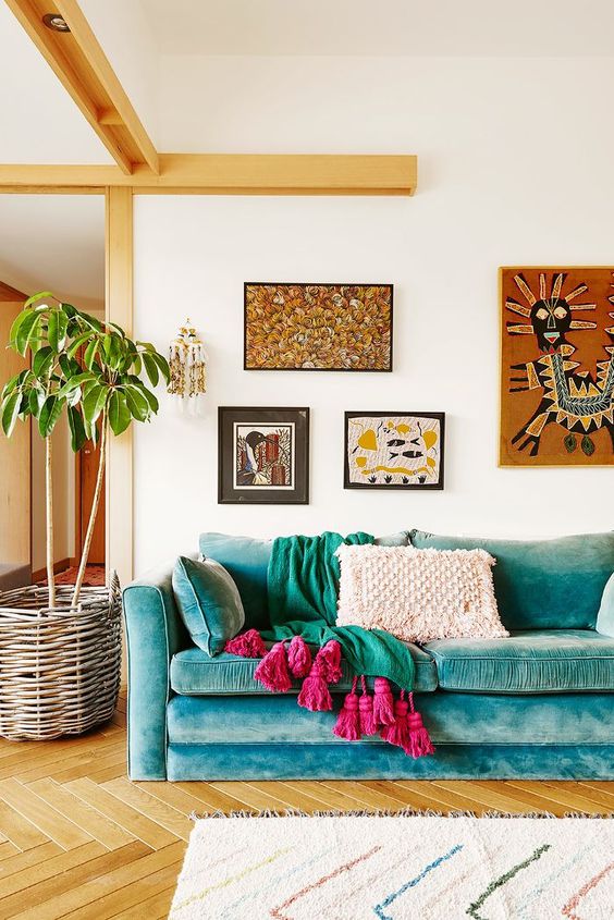 a bright boho living room with a turquoise sofa, bright textiles, a bright boho gallery wlal and a potted plant in a basket
