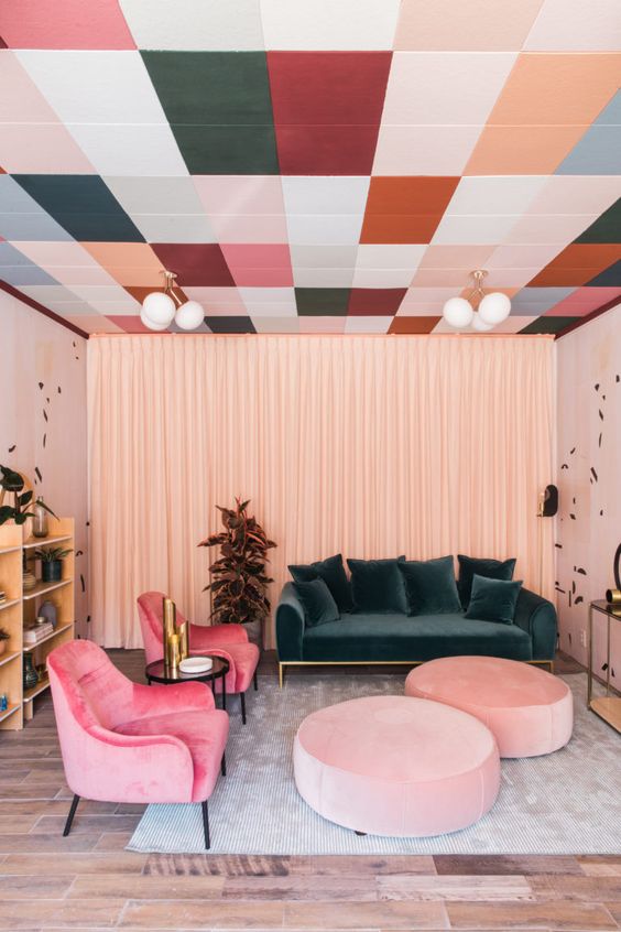 a bright living room with a printed colorful ceiling, a dark green sofa, bright pink chairs and light pink ottomans