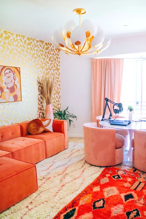a bright maximalist home office with a gold stencild wall, a desk for several people, pink chairs, a coral sectional and bold rugs