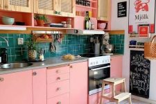 a bright maximalist kitchen with rattan and pink cabinets, a green tile backsplash, a bright printed rug and colorful art