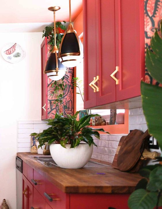 a chic maximalist kitchen with red cabinetry, butcherblock countertops, retro pendant lamps and lots of potted plants