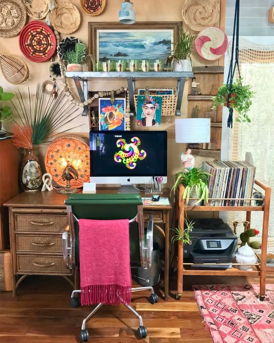 a colorful home office with tan walls, a rattan desk and a cart, colorful decorative baskets and a boho rug plus a pink chair cover