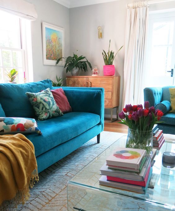 a colorful living room with dove grey walls, a turquoise sofa, bright pillows and accessories, an acrylic coffee table and bold blooms