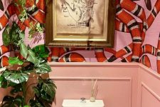 a colorful maximalist bathroom with pink paneling, snake print wallpaper,  potted plants and a bold artwork is creative