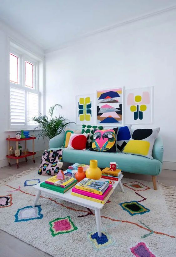 A colorful retro inspired living room with a turquoise sofa, a colorful rug, a gallery wall, pillows and books fill the space with bright colors