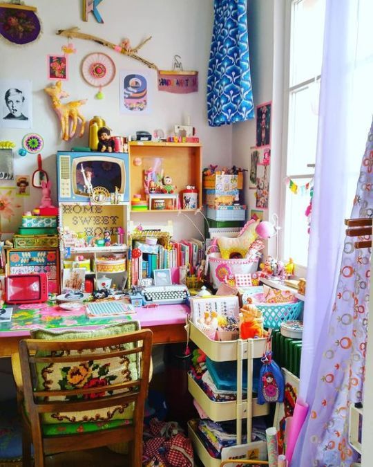 a crazily boho maximalist home office with a hot pink desk, a green chair, colorful textiles, accessories and decor is amazing