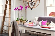 a fancy and whimsy home office with a grey sofa and woven chair, a large desk, a sphere chandelier, a ladder and colorful touches