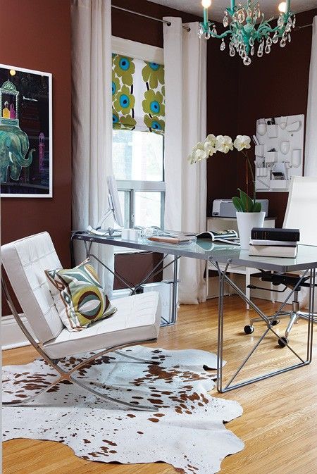a fancy home office with an industrial desk, chic white chairs, black and burgundy walls, a turquoise chandelier and a printed shade
