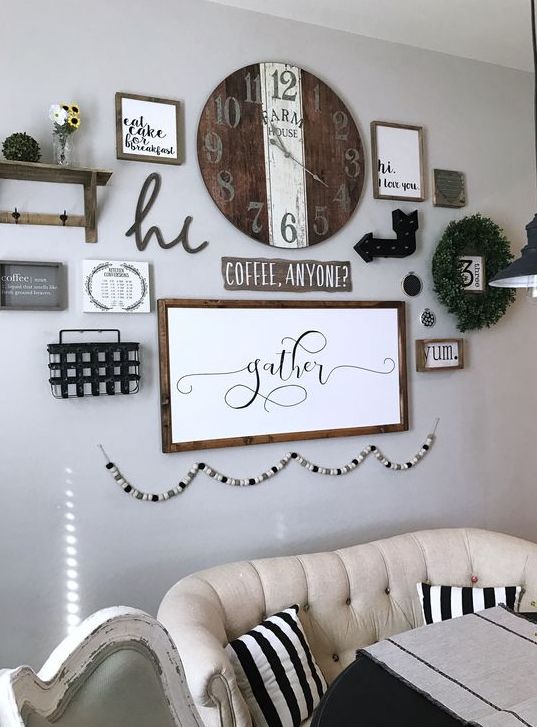 a farmhouse gallery wall with a shelf, a greenery wreath, arrows, a wooden clock, some signs in frames and a wooden bead garland is cool