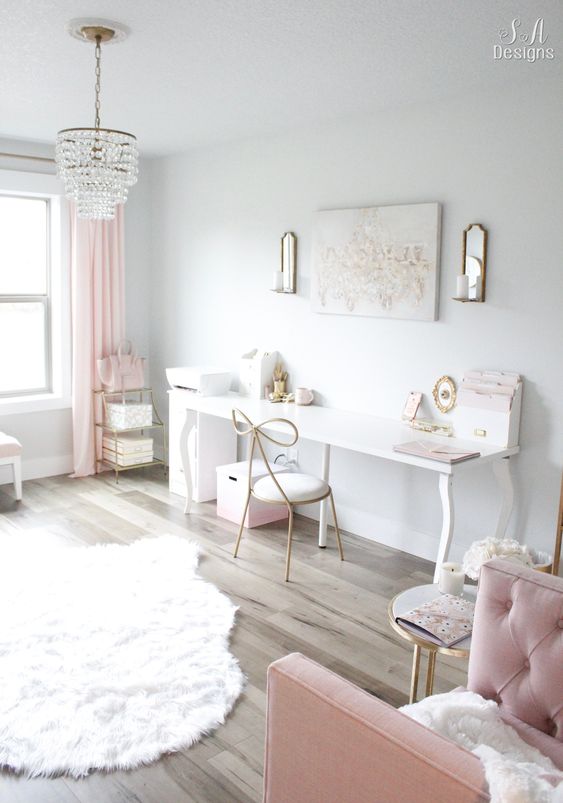 a glam and girlish home office in neutrals, with a desk and a whimsy chair, pink textiles and a tufted armchair, a crystal chandelier and a pretty rug