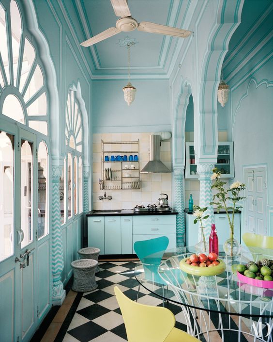 a light blue Moroccan style kitchen with black countertops, a checked floor, a round glass table, yellow and blue chairs