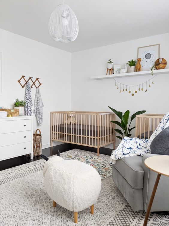 a lvoely neutral nursery with stained cribs, a grey chair, an animal-shaped ottoman, a white dresser, a shelf with artworks