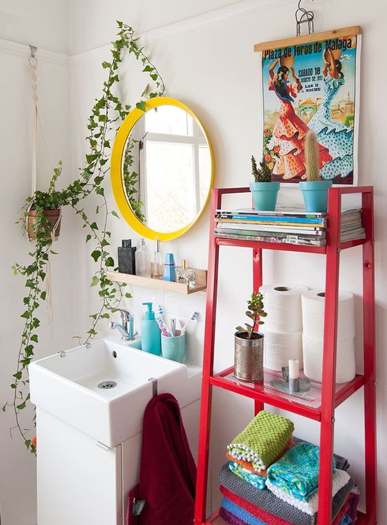 a maximalist bathroom with a yellow frame mirror, a red ladder with decor and a colorful artwork plus potted greenery