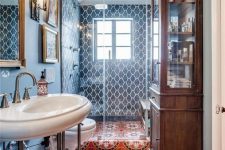 a maximalist bathroom with blue walls and blue tiles, a red mosaic tile floor, a stained storage cabinet and a smal gallery wall
