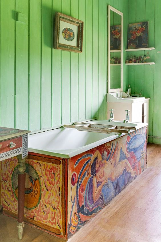 a maximalist bathroom with green planked walls, a colorful bathtub, a painted sink stand, pretty artworks and chic