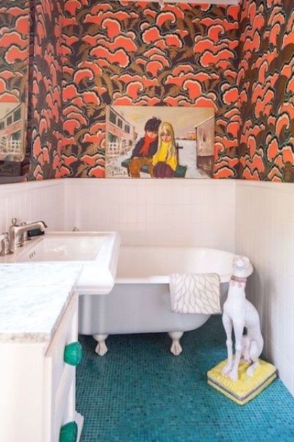 a maximalist bathroom with white paneling and bold printed wallpaper, blue tiles on the floor, with artworks and a dog