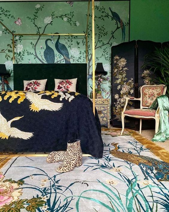 a maximalist bedroom with green walls with painting, a dark bed and a screen, a refined chair and amazing printed textiles that add chic