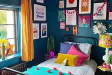 a maximalist guest bedroom with a metal bed, navy walls, a colorful gallery wall, a bright floral lamp and yellow curtains, colorful bedding