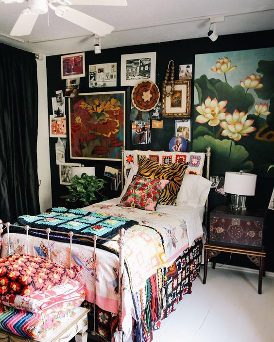 a maximalist guest bedroom with black walls, a metal bed, a refined inlaid nightstand, a bold gallery wall and colorful textiles