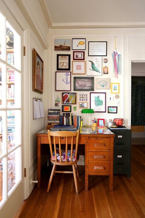 a maximalist home office wiht a vintage desk and chair, a colorful gallery wall and bold books and a table lamp