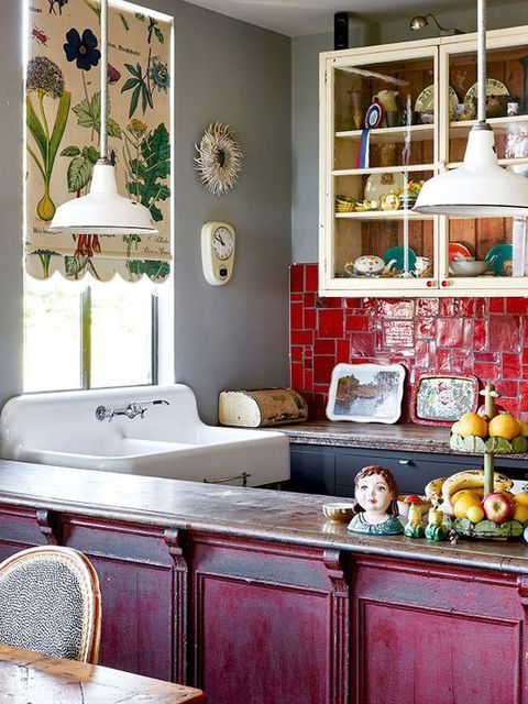 a maximalist kitchen with a hot pink kitchen island, red tiles on the backsplash, a botanical curtain and creamy and black cabinets