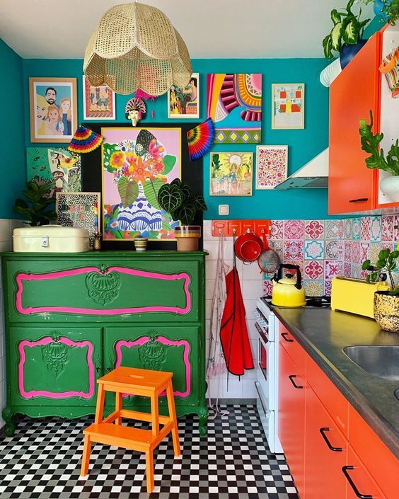 a maximalist kitchen with teal walls, red cabinets, a green dresser, a colorful gallery wall and a checked floor