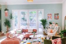 a maximalist living room with a green accent wall, a pink sofa, a green chair, a bright rug and a glazed tiered table