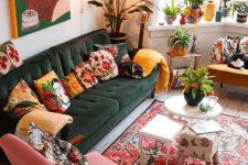 a maximalist living room with a green sofa and mustard and pink chairs, a bold rug and colorful pillows, potted plants and candleholders