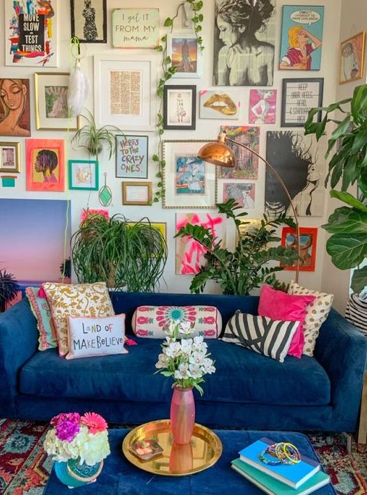 a maximalist living room with a large and bold gallery wall, with a bold blue sofa, statement plants and a brass lamp and a tray