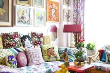a maximalist living room with a pink sofa and a coffee table, a floral chair, a bright gallery wall and potted plants and blooms