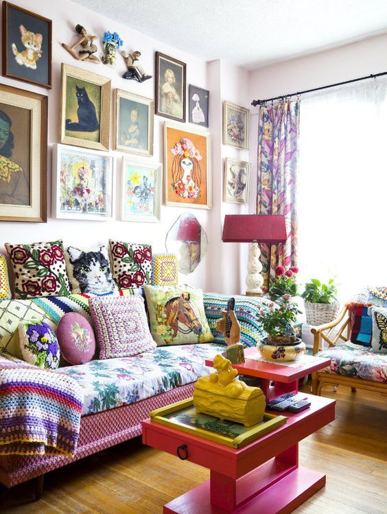 a maximalist living room with a pink sofa, table and lamp, a colorful gallery wall, bold upholstery and pillows plus various plants