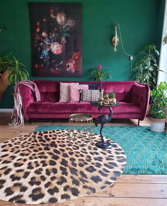 a maximalist living room with green walls, layered rugs, a fuchsia sofa, a bold artwork and potted greenery is chic