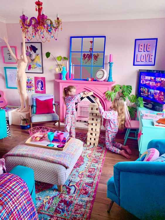 a maximalist living room with light pink walls, a hot pink fireplace, blue furniture and colorful textiles, a pink chandelier and a colorful gallery wall