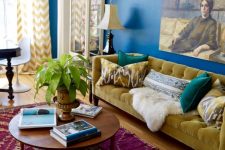 a maximalist living room with navy walls, a fuchsia printed rug, a mustard sofa and blue chairs and a bold artwork