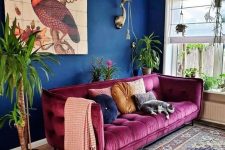 a maximalist living room with navy walls, a fuchsia sofa, a bold printed rug, potted plants and a lovely artwork is chic