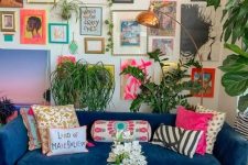 a maximalist living room with neutral walls, a blue sofa and a matching ottoman, a colorful gallery wall and lots of potted plants