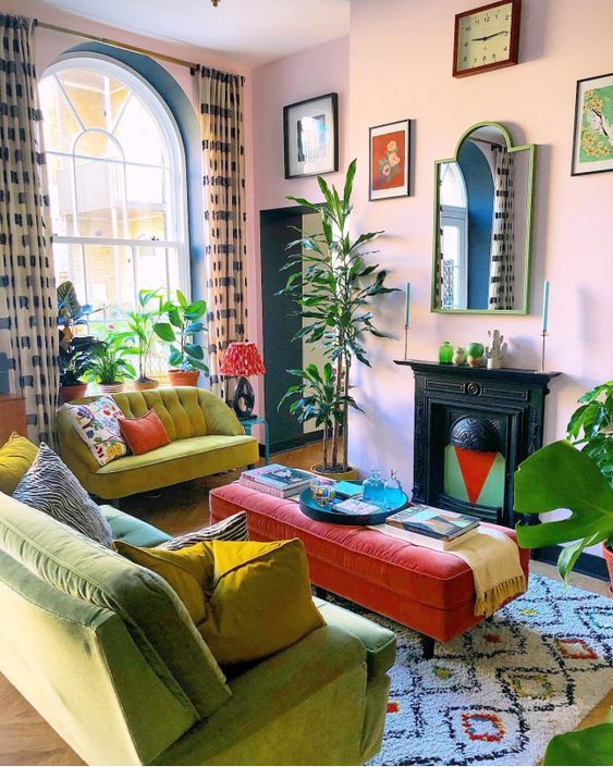 a maximalist living room with pink walls, a non-working fireplace, a green and mustard sofa, colorful artworks and printed textiles