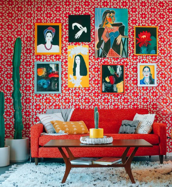 a maximalist living room with red printed wallpaper, a red sofa, potted cacti, a colorful gallery wall and a coffee table