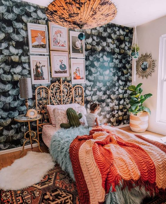 A maximalist sleeping space with a dark accent wall, a rattan bed, a catchy pendant lamp and bright textiles for creating a mood