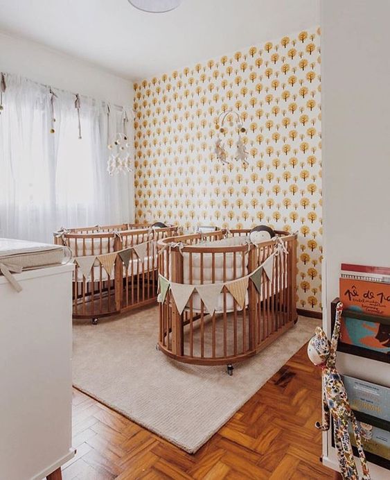 A mid century modern nursery with an accent wall, matching cribs and buntings, a changing table and matching mobiles