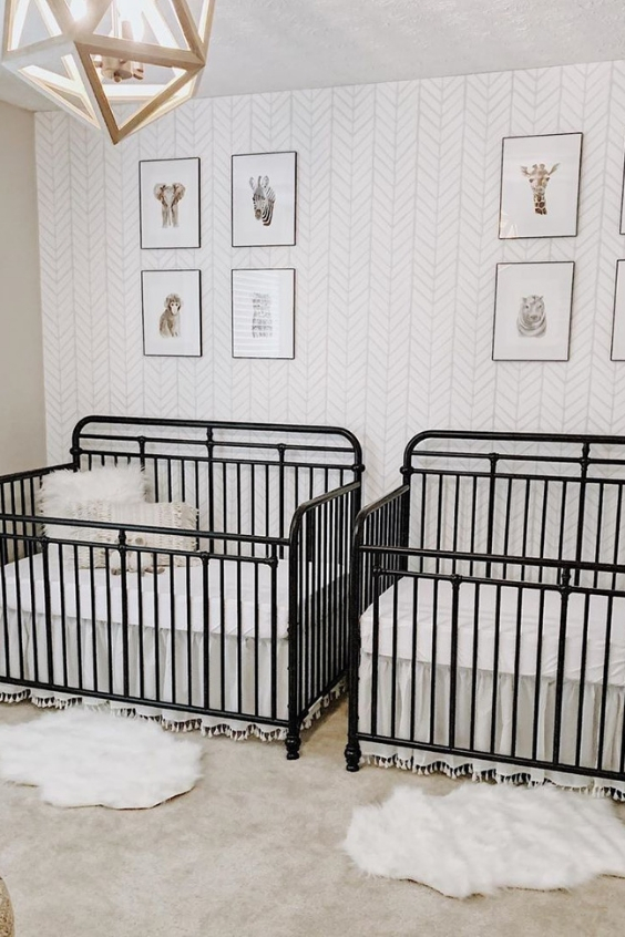 A mid century modern nursery with an accent wallpaper wall, black metal cribs, a geometric lamp and layered rugs