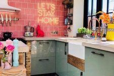 a modern maximalist kitchen with aqua cabinets, a pink tile backsplash, a neon light, a black window frame and colorful vases