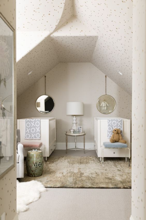 a neutral attic nursery with neutral cribs, printed bedding, polka dot wallpaper all over the space and layered rugs