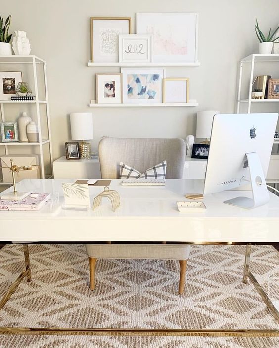 a neutral fancy home office with a desk, open shelving units, a ledge gallery wall and a printed rug plus matching table lamps